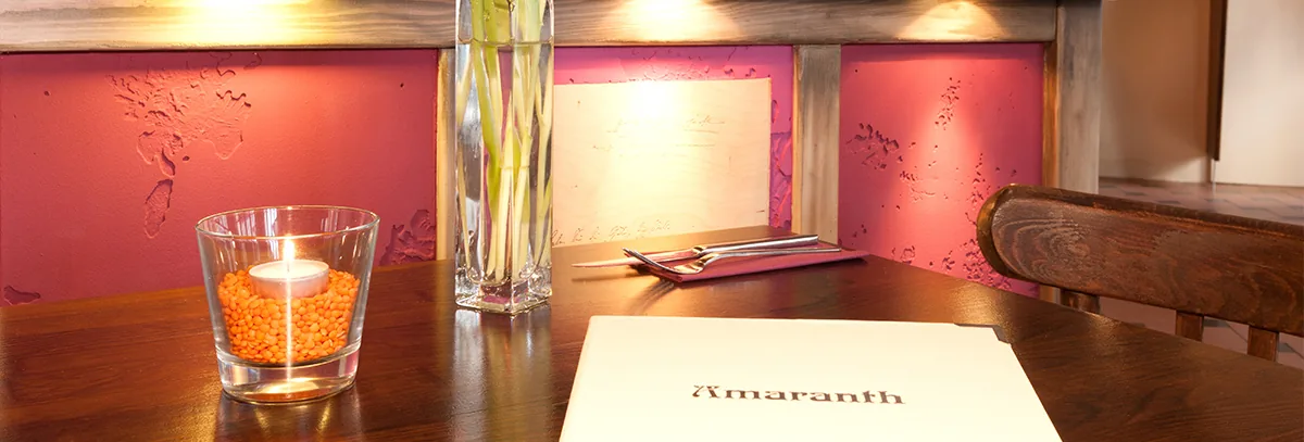 Speisekarte und Kerze auf dunklem Holztisch vor beerenfarbener Wand